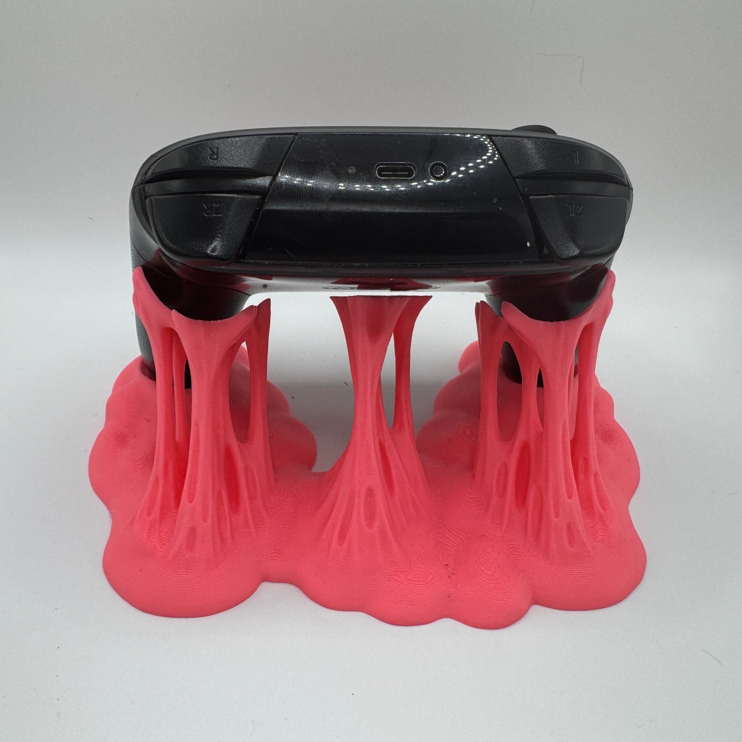 Black electronic device with a USB port on a pink plastic goo stand against a white background