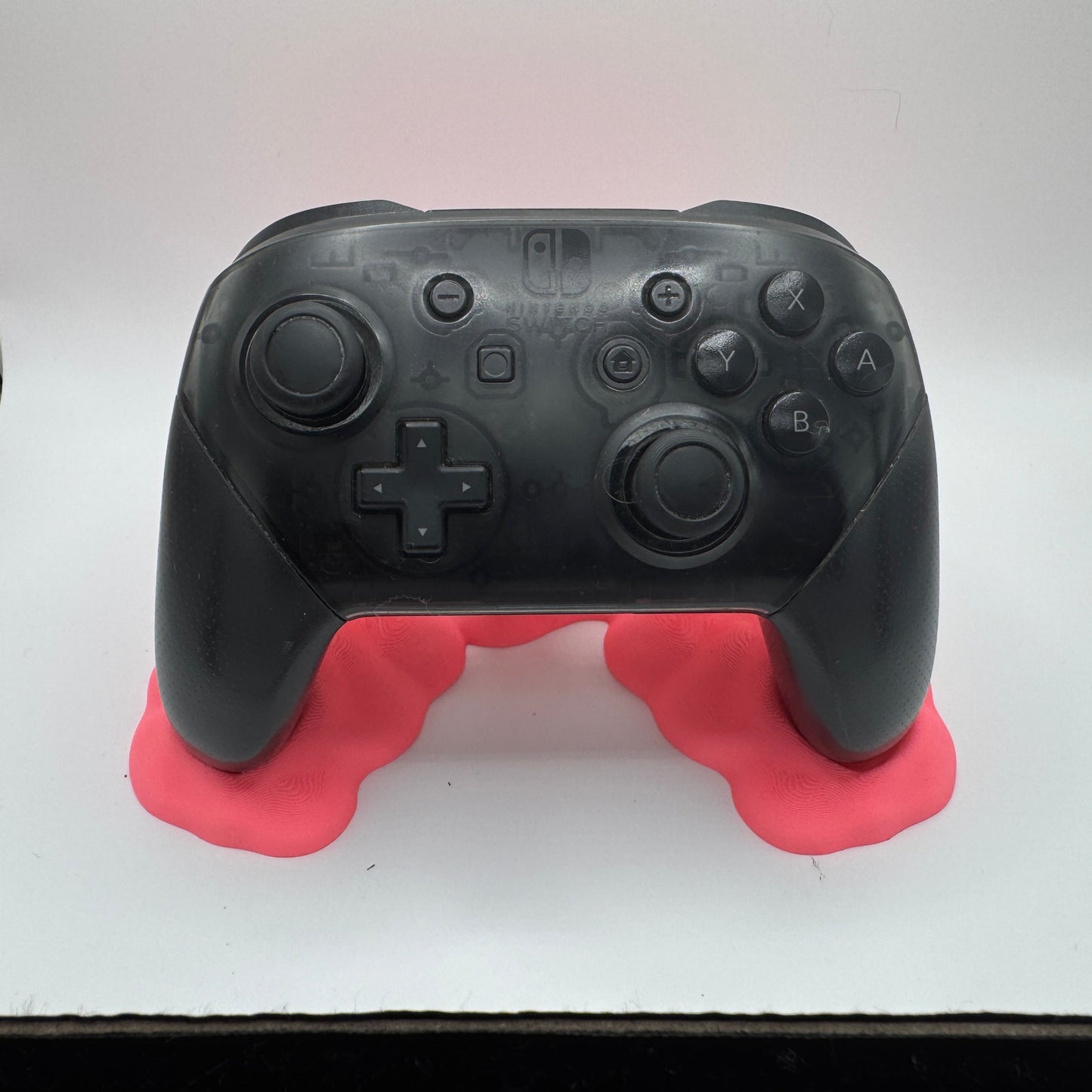 Black gaming controller on a pink stand against a white background