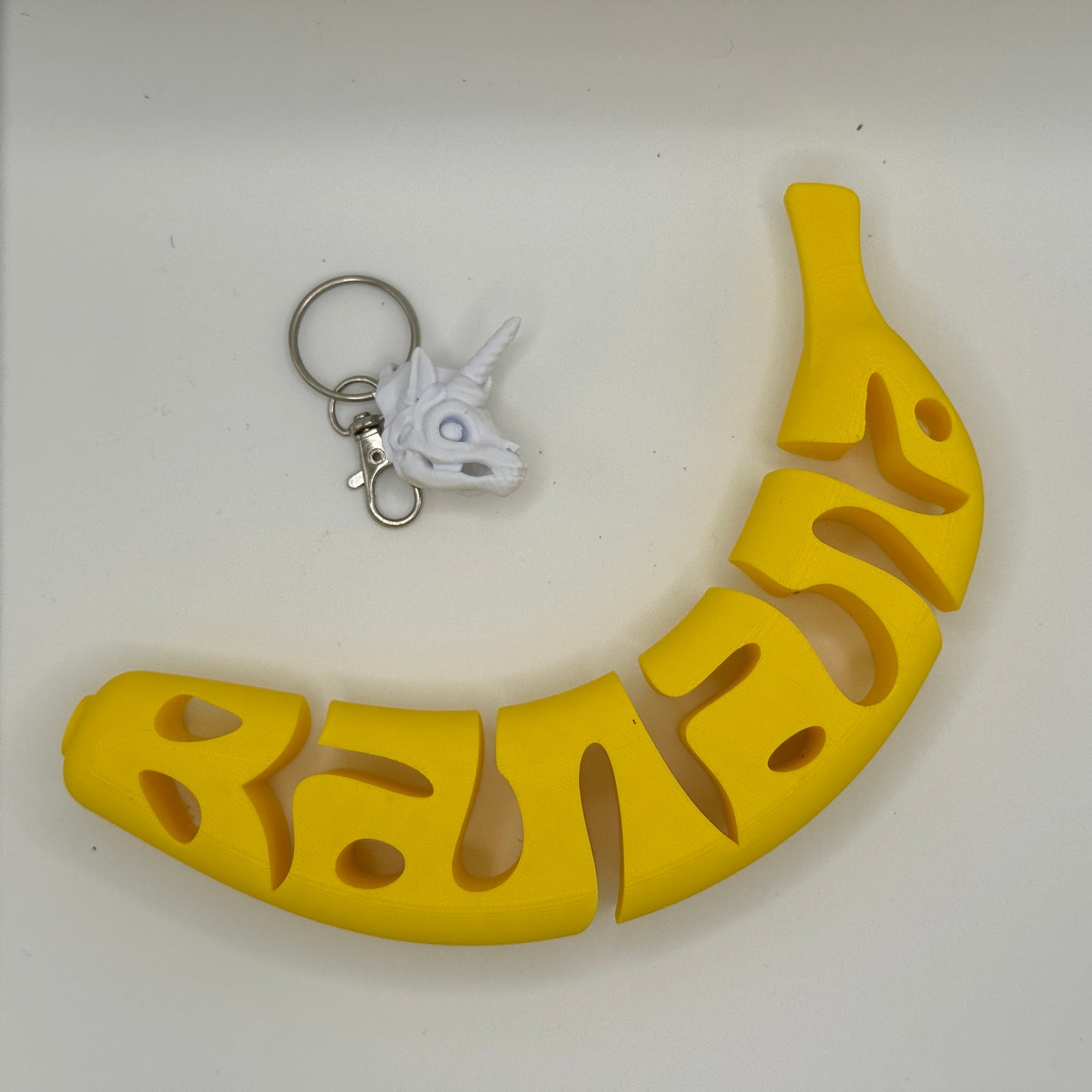 Yellow banana- near a small white unicorn charm on a light gray background
