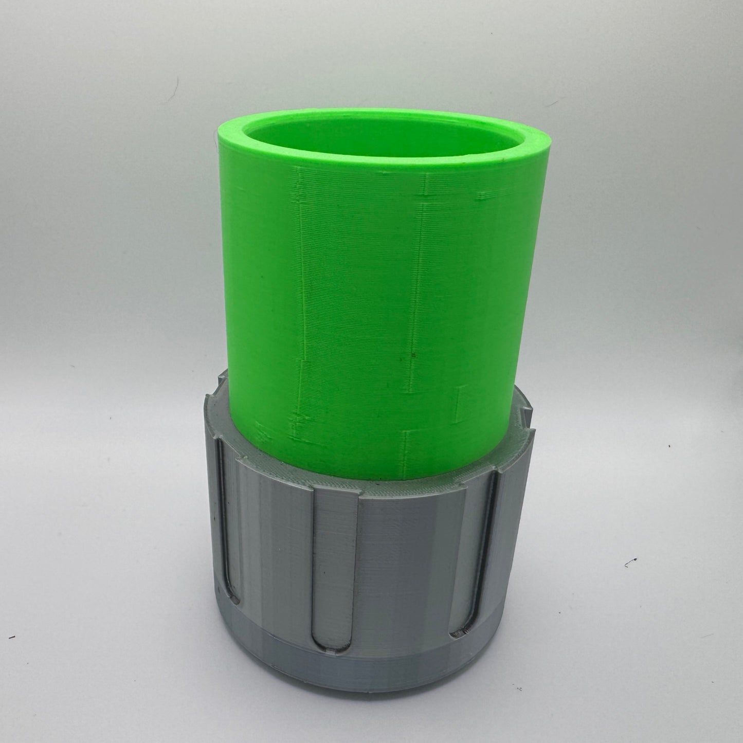 A 3D-printed container with a bright green cylindrical upper section and a gray lower base featuring vertical grooves. The object is hollow, with an open top, and is set against a plain light gray background.