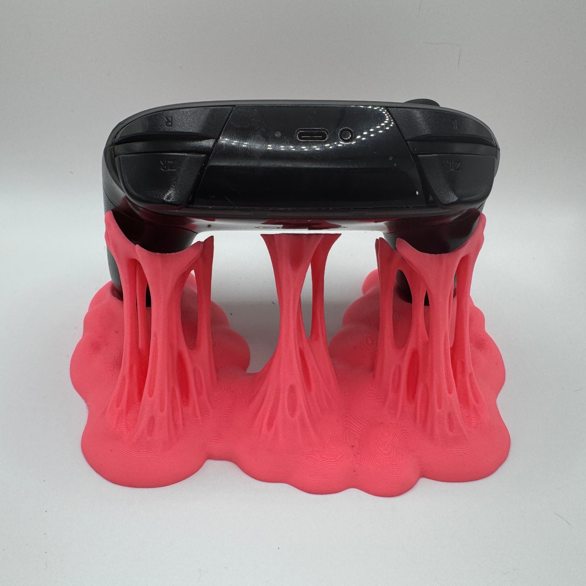 Black electronic device with a USB port on a pink plastic goo stand against a white background