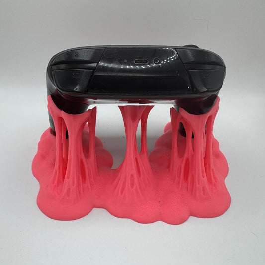 Black electronic device with a USB port on a pink plastic goo stand against a white background