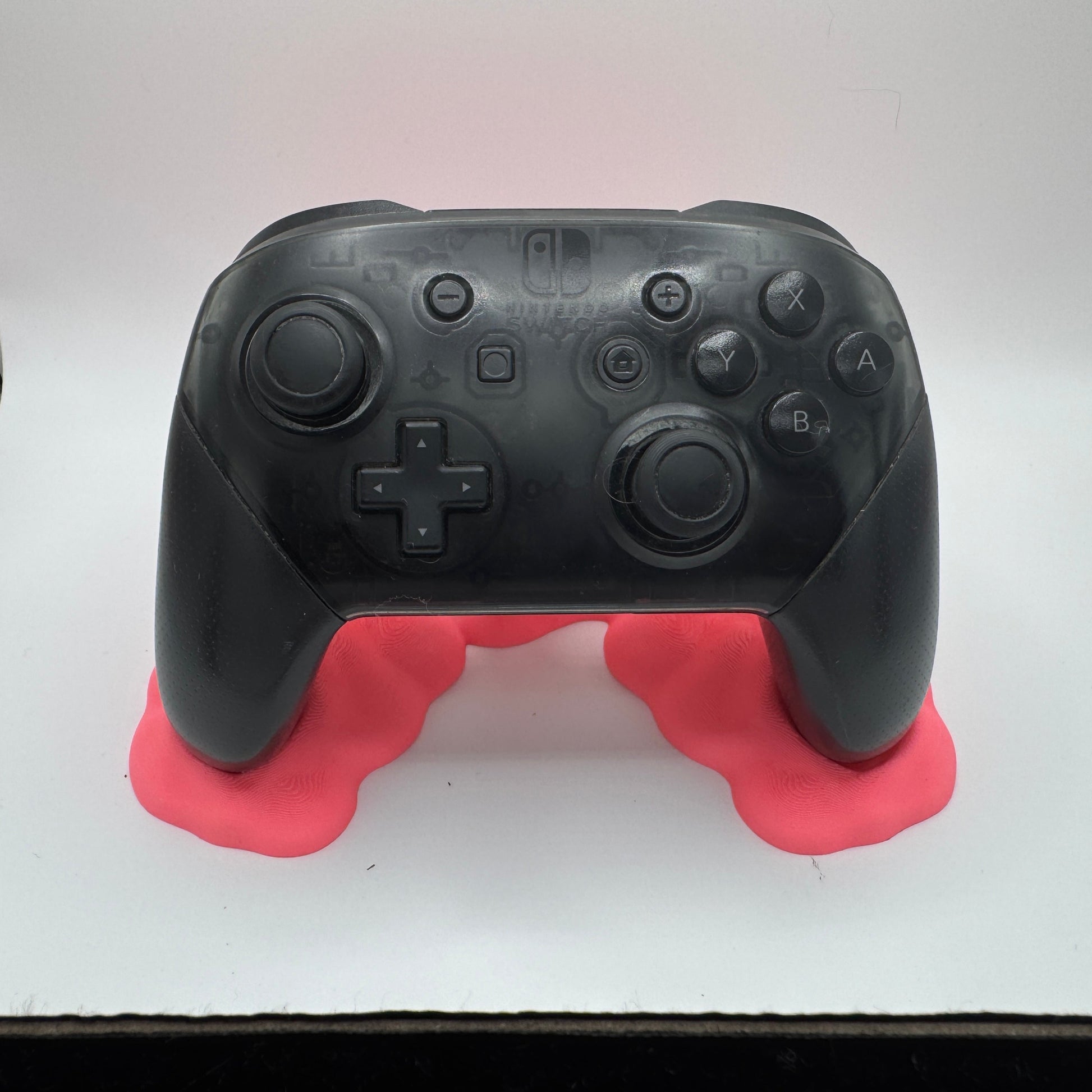 Black gaming controller on a pink stand against a white background