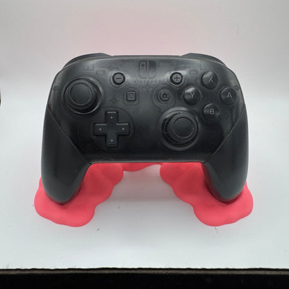 Black gaming controller on a pink stand against a white background