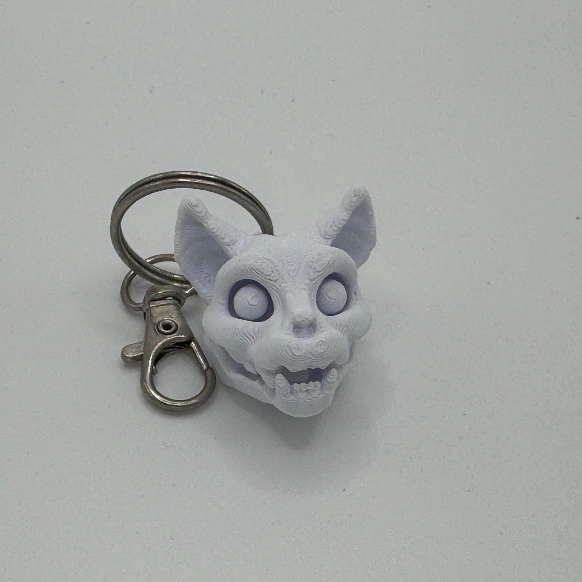 Keychain with a white cat-like creature head on a light gray background