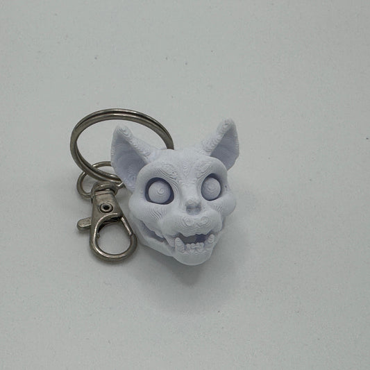 Keychain with a white cat-like creature head on a light gray background