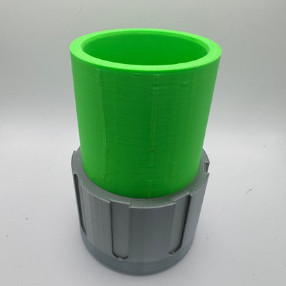 A 3D-printed container with a bright green cylindrical upper section and a gray lower base featuring vertical grooves. The object is hollow, with an open top, and is set against a plain light gray background.
